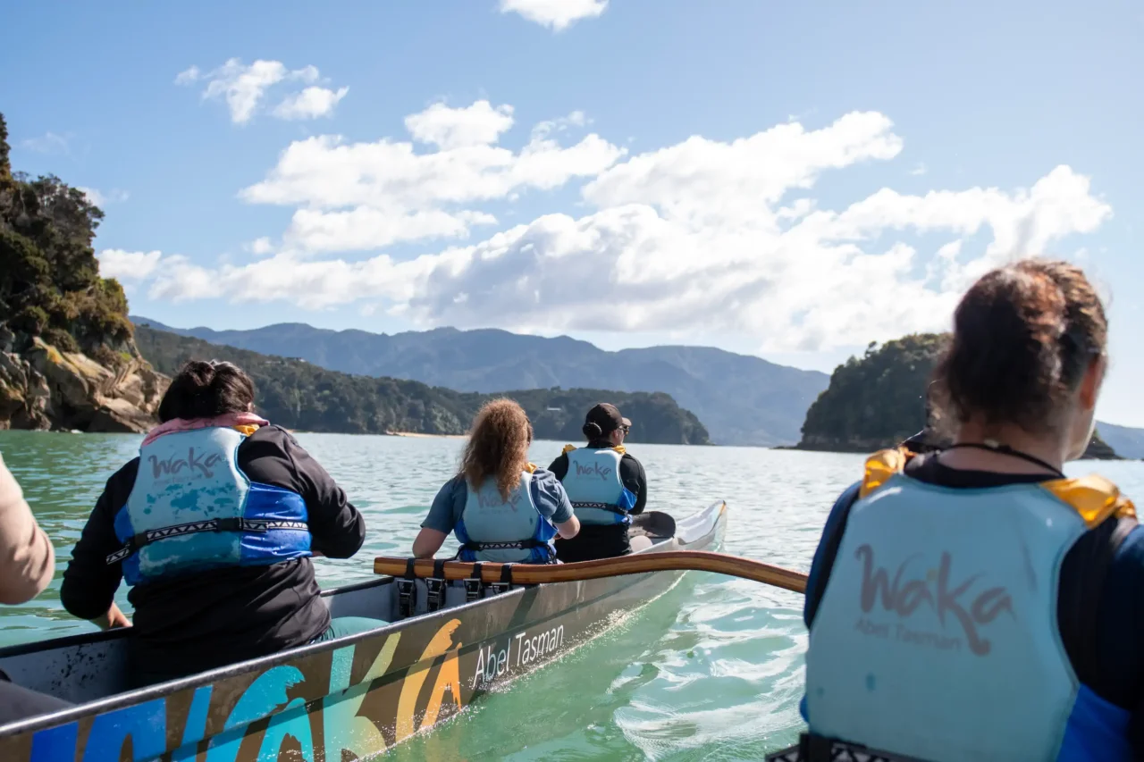 Paddlers paddling a double hulled waka towards Split Apple Rock