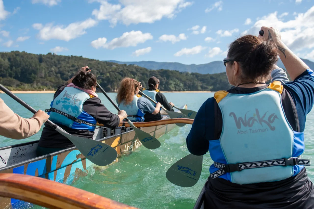 Paddlers paddling a double hulled waka towards Split Apple Rock