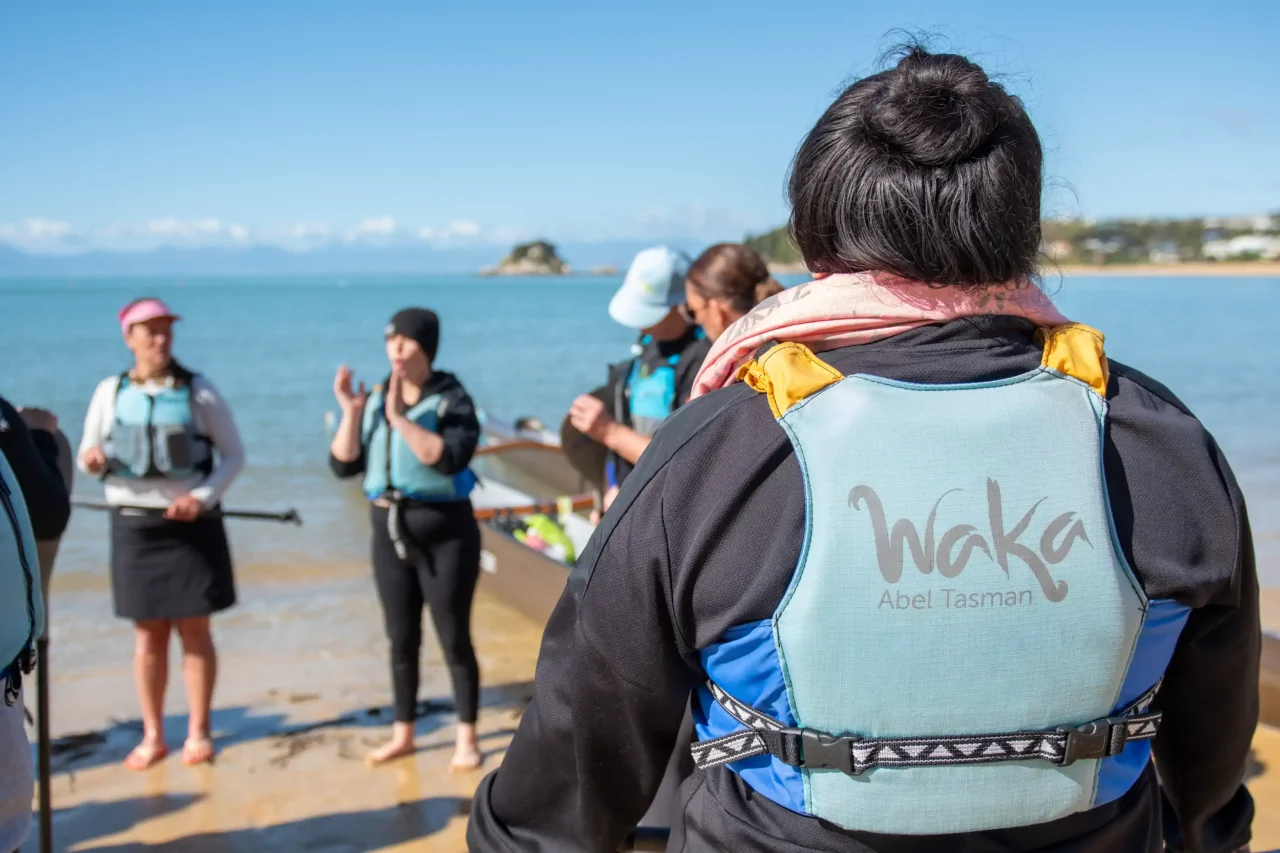 Hana explaining about the waka to new crew on the beach at Kaiteretere